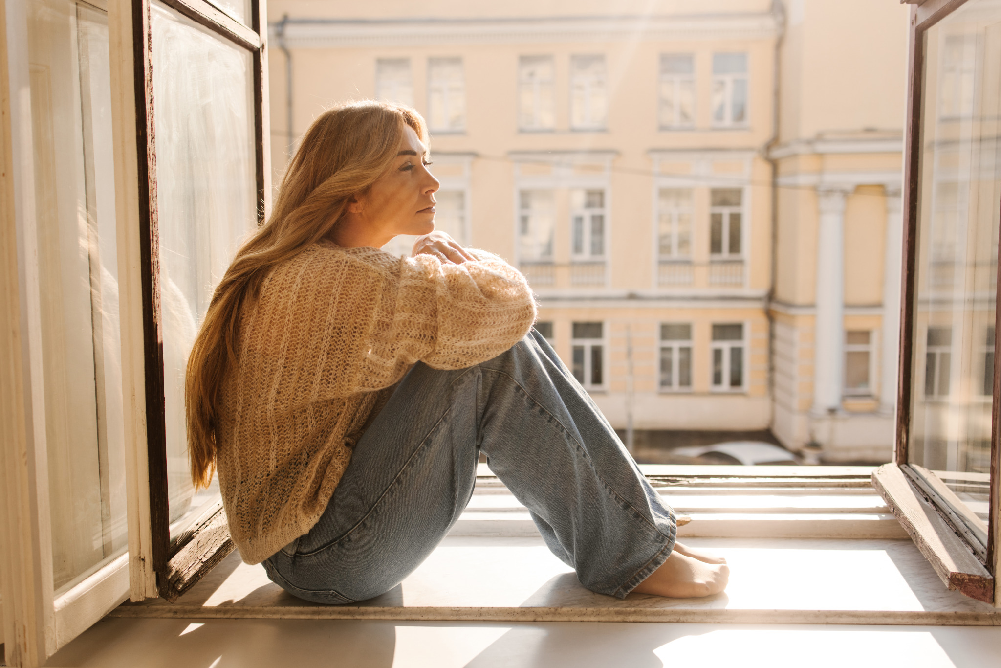 sad-fairskinned-adult-woman-blonde-warm-sweater-jeans-sitting-windowsill-sunny-day-mood-concept